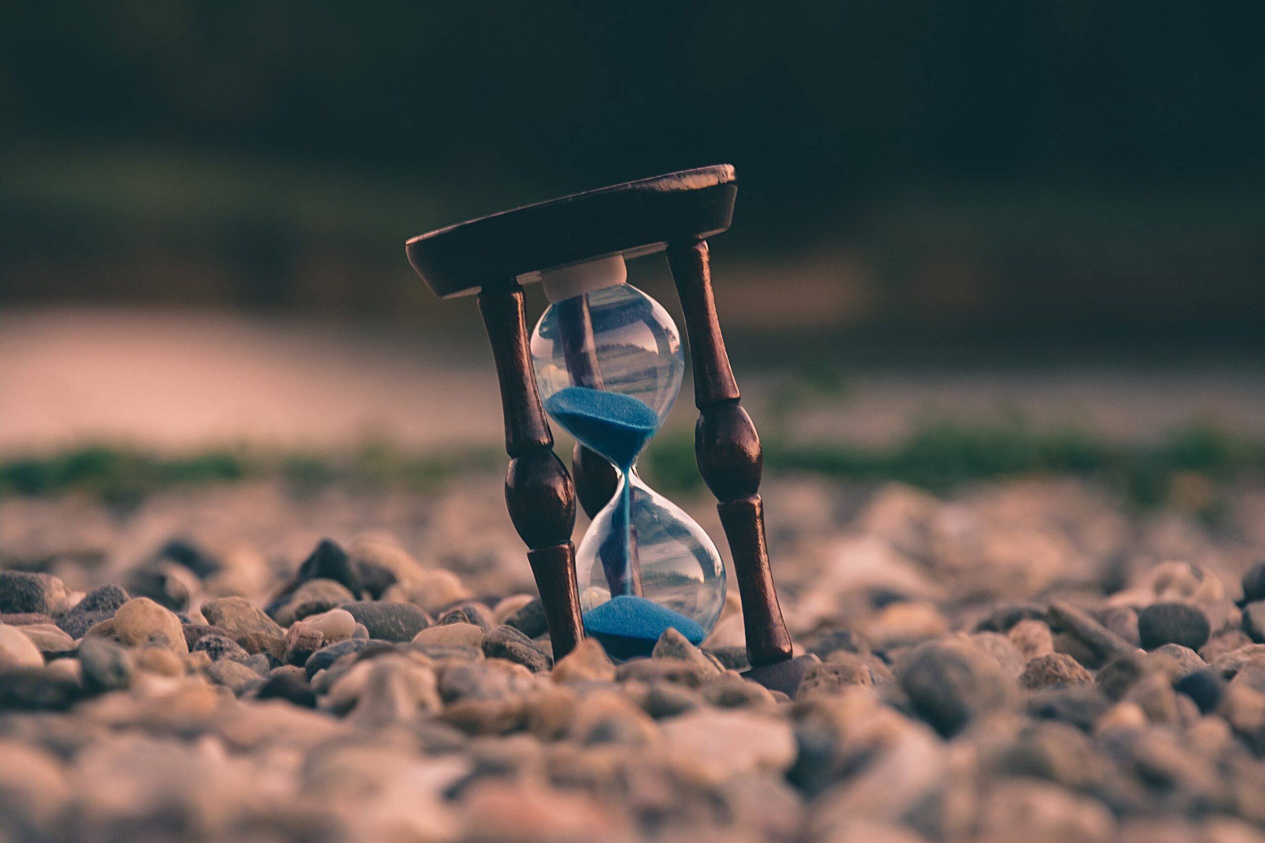 Hourglass with blue sand on pebble beach